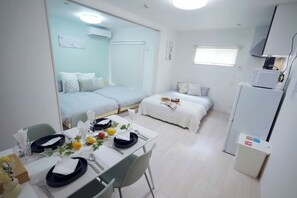 Une chambre d’hôtel de taille réduite comprenant un coin repas, deux lits, un réfrigérateur et une fenêtre.