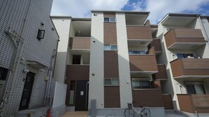 A modern multi-story residential building with balconies, a bicycle parked in front, and a gated entrance. - WANO (Osaka)