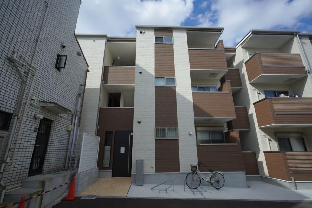 A modern multi-story residential building with balconies, a bicycle parked in front, and a gated entrance.