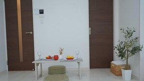 A minimalist room with a white table set for two, two round ottomans, a potted plant, and a basket. - WANO (Osaka)