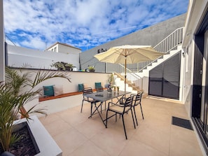An outdoor patio with a table and chairs, a staircase, and a covered area with an umbrella.