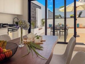 A modern kitchen with a dining area, a large window, and a view of the outdoor patio.