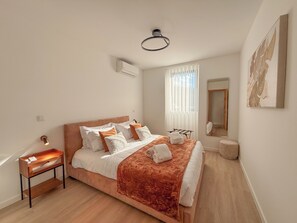 A bedroom with a bed, bedside table, air conditioning unit, window with curtains, and a mirror.