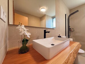 A bathroom with a white sink, a black faucet, a glass vase with white flowers, and a wooden countertop.