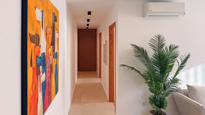 Un couloir au design moderne, agrémenté d’un grand tableau abstrait, d’une plante en pot et d’un système de climatisation intégré.