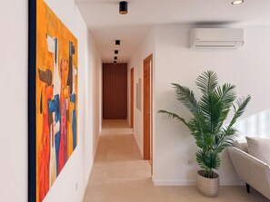 Un pasillo con diseño moderno, que presenta un cuadro abstracto grande, una planta en maceta y un equipo de aire acondicionado empotrado.