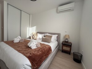 A neatly made bed with towels, a bedside lamp, and a waste basket in a hotel room.