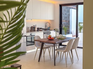 A modern kitchen with white cabinets, a dining table with chairs, and a view of the outdoors through a glass door.