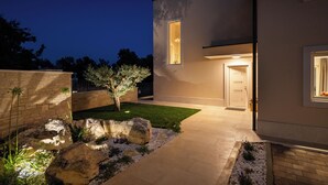 A modern house with a well-lit entrance, a small garden with rocks and plants, and a paved driveway. - Luxury villa for 8 persons with swimming pool, whirlpool and sauna (Nova Vas)