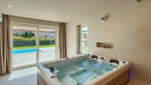 A modern bathroom with a large bathtub, a shower area, and a glass door leading to a pool. - Luxury villa for 8 persons with swimming pool, whirlpool and sauna (Nova Vas)