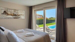 A bedroom with a bed, a painting on the wall, a TV, and a view of a pool and garden. - Luxury villa for 8 persons with swimming pool, whirlpool and sauna (Nova Vas)