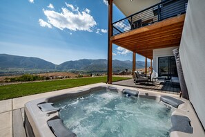 Ein Whirlpool mit Blick auf die Berge, eine Terrasse mit Gartenmöbeln und ein überdachter Bereich mit einem Balkon.
