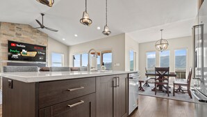 A modern kitchen with a large island, dark wood cabinets, and a flat-screen TV displaying various streaming services. - Mountain View Retreat B11|Hot Tub |Near Powder Mtn (Eden)