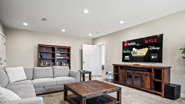 A living room with a grey sofa, a coffee table, a wooden cabinet, and a TV displaying streaming services logos.