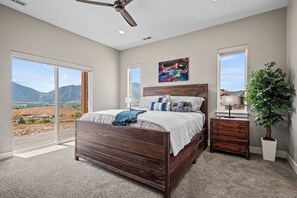 Ein Schlafzimmer mit einem großen Bett, einem Nachttisch, einer Kommode, einem Deckenventilator, einem großen Fenster und einem Gemälde.