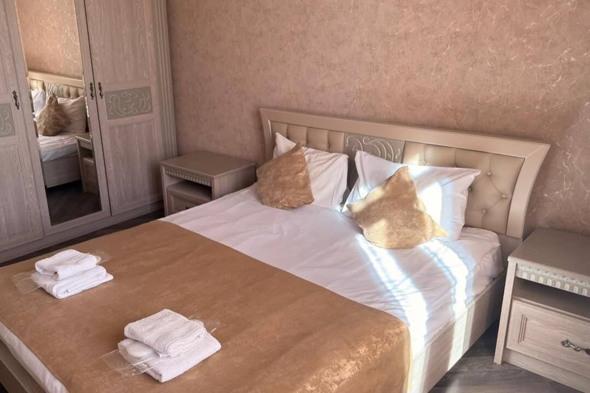 A bedroom with a large bed, a nightstand, a wardrobe, and a mirror.
