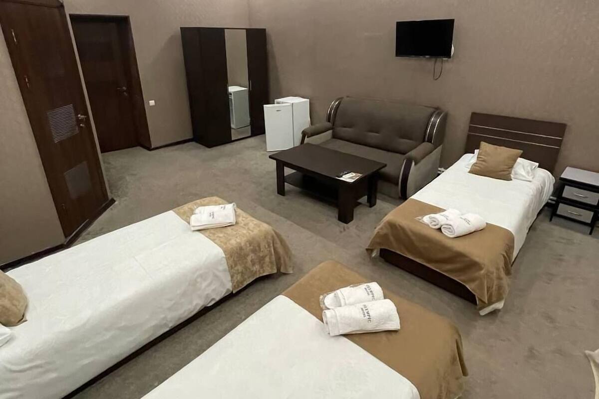 A hotel room with two single beds, a sofa, a small table, a TV, and a wardrobe.