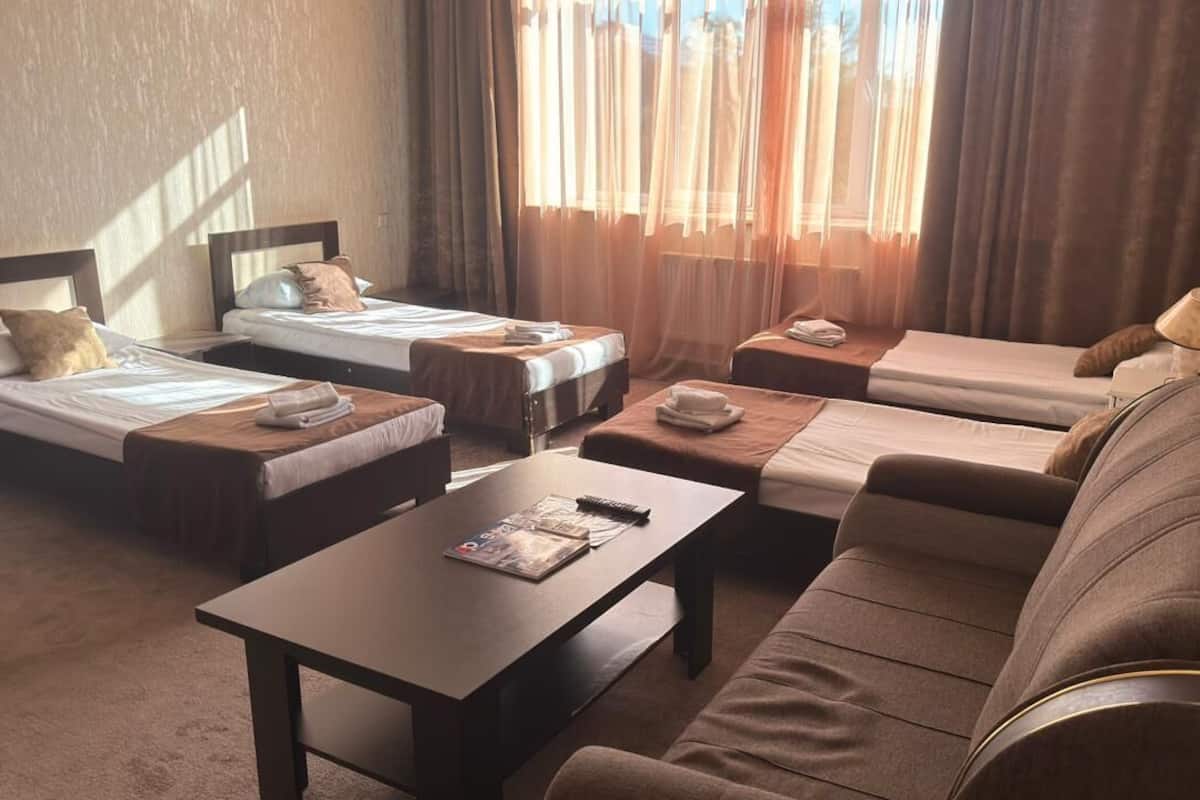 A hotel room with two single beds, a sofa, a coffee table, and a lamp.