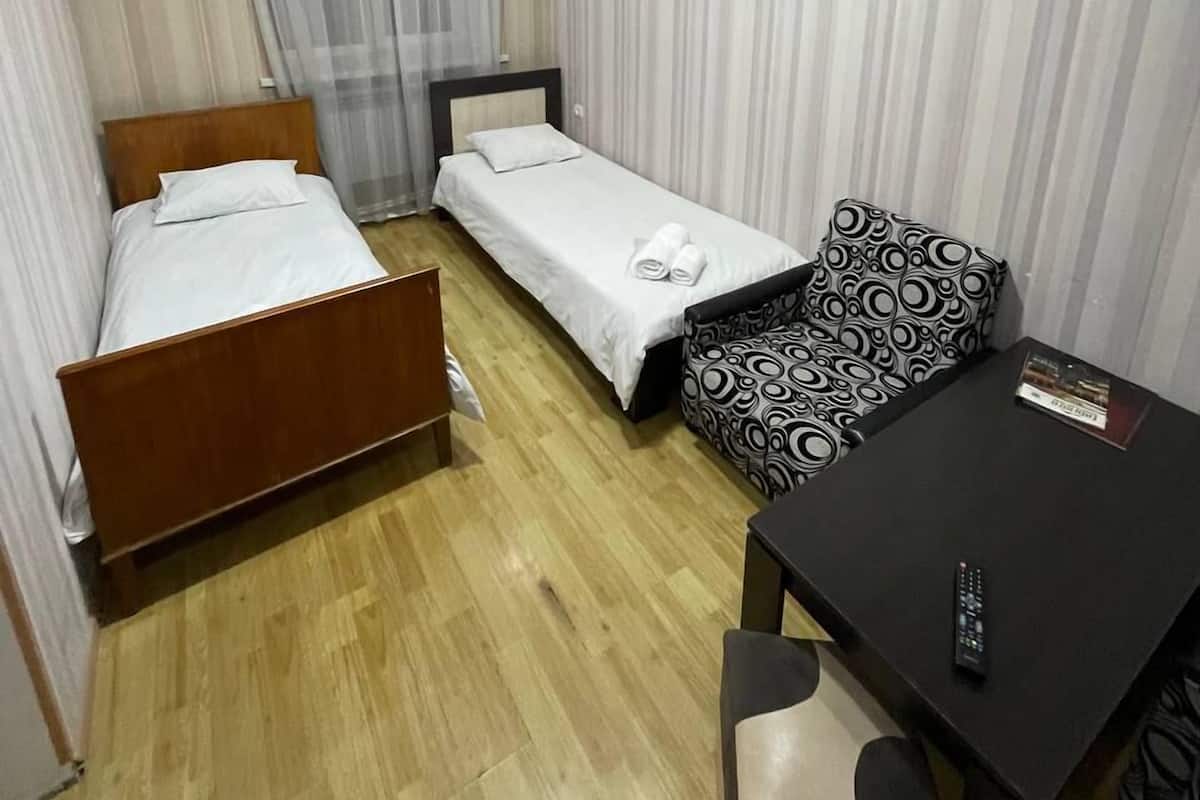 A hotel room with two single beds, a sofa, a small table, and a TV.
