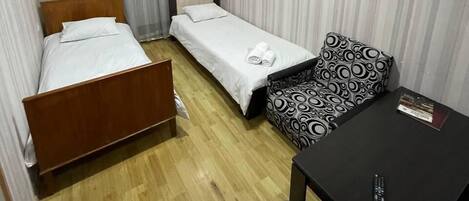 Habitación de hotel con dos camas individuales, un sofá, una mesita y un televisor.