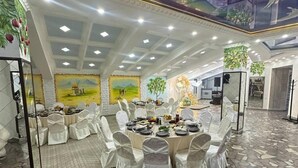 Un amplio salón de banquetes con mesas redondas, sillas blancas y un mural en el techo.