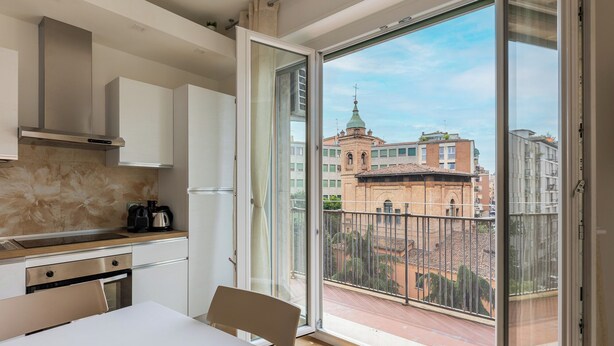 A modern kitchen with a large window, a dining area, and a view of buildings. - Bologna city center view by Wonderful Italy (Bologna)