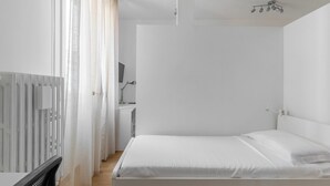 A minimalist bedroom with a bed, a radiator, and a desk with a lamp. - Bologna city center view by Wonderful Italy (Bologna)