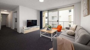 A modern living room with a flat-screen TV, a coffee table, a sofa, and a balcony with a view of the city. - Beachfront Bliss 2BR Ocean Breeze Hideaway,Parking (Surfers Paradise)