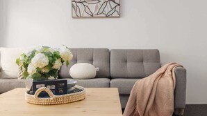 A living room with a grey sofa, a wooden coffee table with a woven basket, and a white cushion. - Beachfront Bliss 2BR Ocean Breeze Hideaway,Parking (Surfers Paradise)