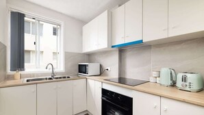 A modern kitchen with white cabinets, a microwave, a toaster, and a sink. - Beachfront Bliss 2BR Ocean Breeze Hideaway,Parking (Surfers Paradise)