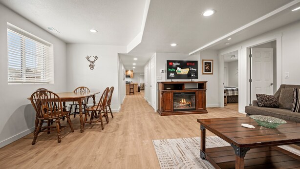 A modern living room with a fireplace, a dining area with wooden chairs, and a flat-screen TV mounted on the wall displaying various streaming services. - Grand Ogden Lodge, Hot Tub, Close to Ski Resorts – 6 BR | 5 Baths | Hot Tub (North Ogden)