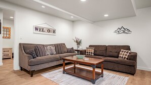 A modern living room with a brown sofa set, a wooden coffee table, and a 'WELCOME' sign on the wall. - Grand Ogden Lodge, Hot Tub, Close to Ski Resorts – 6 BR | 5 Baths | Hot Tub (North Ogden)