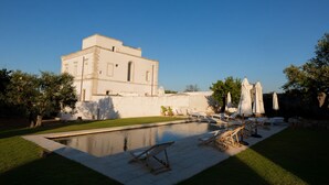 A pool area with lounge chairs and umbrellas, a building with a flat roof, and a clear sky. - Masseria Monet (Monopoli)