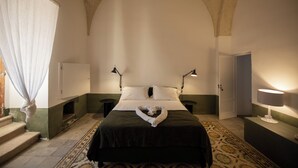 A bedroom with a bed, two bedside lamps, a nightstand, a dresser, a patterned rug, and a window with curtains. - Masseria Monet (Monopoli)
