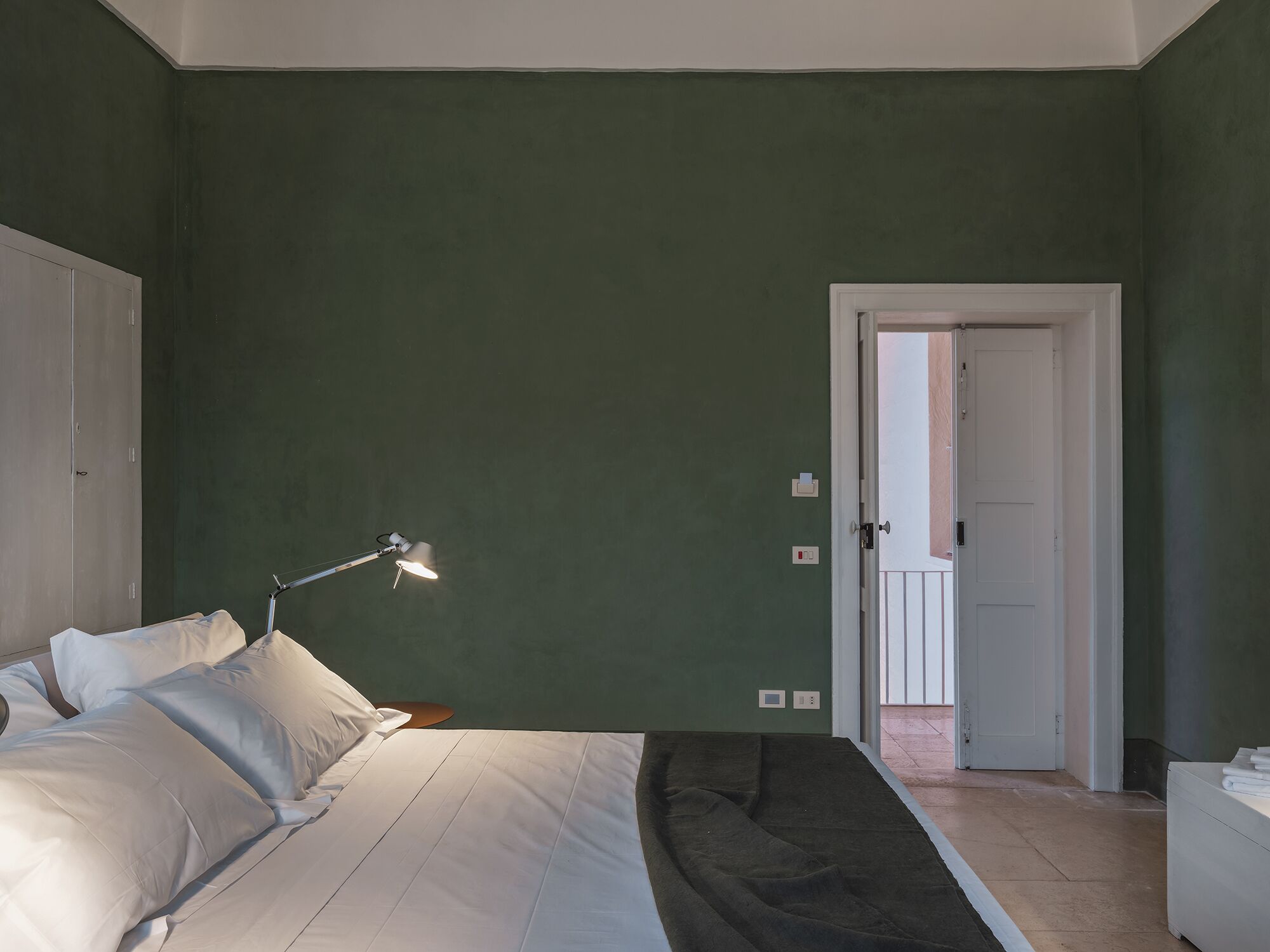 A bedroom with a bed, a bedside lamp, and a door leading to another room.