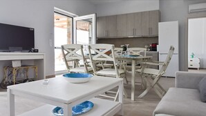 A modern living room with a white sofa, a dining table with chairs, a TV, and a kitchen area with cabinets and a refrigerator. - Lena Apartment Kea (Otzias Kea)