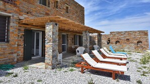 A stone building with a covered patio area, outdoor seating, and lounge chairs. - Lena Apartment Kea (Otzias Kea)