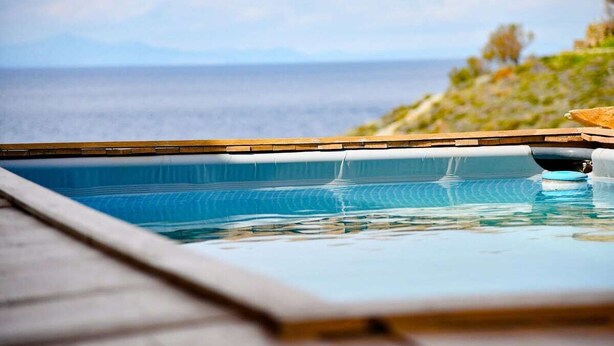 A swimming pool with a wooden deck and a view of the ocean. - Lena Apartment Kea (Otzias Kea)