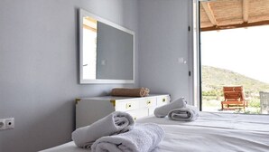A bedroom with a bed, a dresser, a mirror, and a view of a hillside. - Lena Apartment Kea (Otzias Kea)