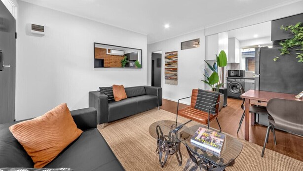 Una sala de estar moderna con sofá, mesa de centro y sillas. Cuenta con una zona de cocina equipada y una mesa de comedor.