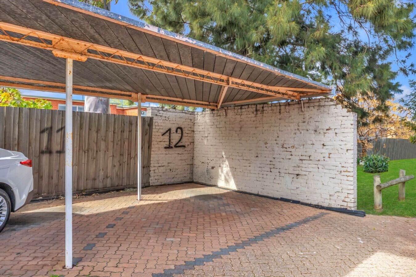 A covered outdoor area with a brick wall, a wooden fence, and a car parked nearby.