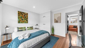 Un dormitorio moderno con una cama grande, un escritorio y un área de estar contigua con un sofá.