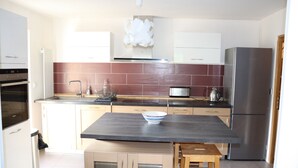 A modern kitchen with a central island, stainless steel appliances, and a red-tiled backsplash.