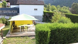 A tent with a table and chairs set up in a garden with a white building in the background.