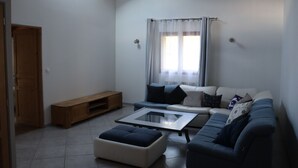 A living room with a sofa, ottoman, and coffee table. There is a wooden bench and a window with curtains.