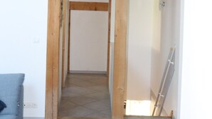 A hallway with exposed wooden beams, a tiled floor, and a blue couch.