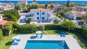 A residential area with a swimming pool, lounge chairs, and a large house with a terrace.