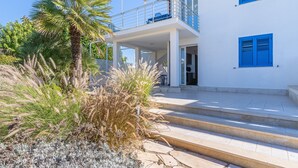 A modern two-story building with a balcony, steps leading to the entrance, and a garden area with various plants.