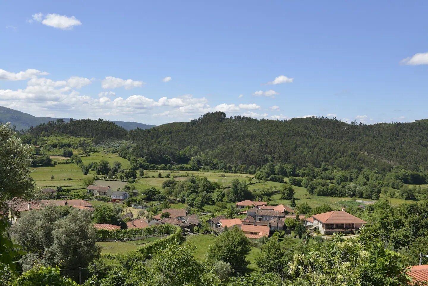 Un pueblo rural con casas y campos, rodeado de colinas boscosas.