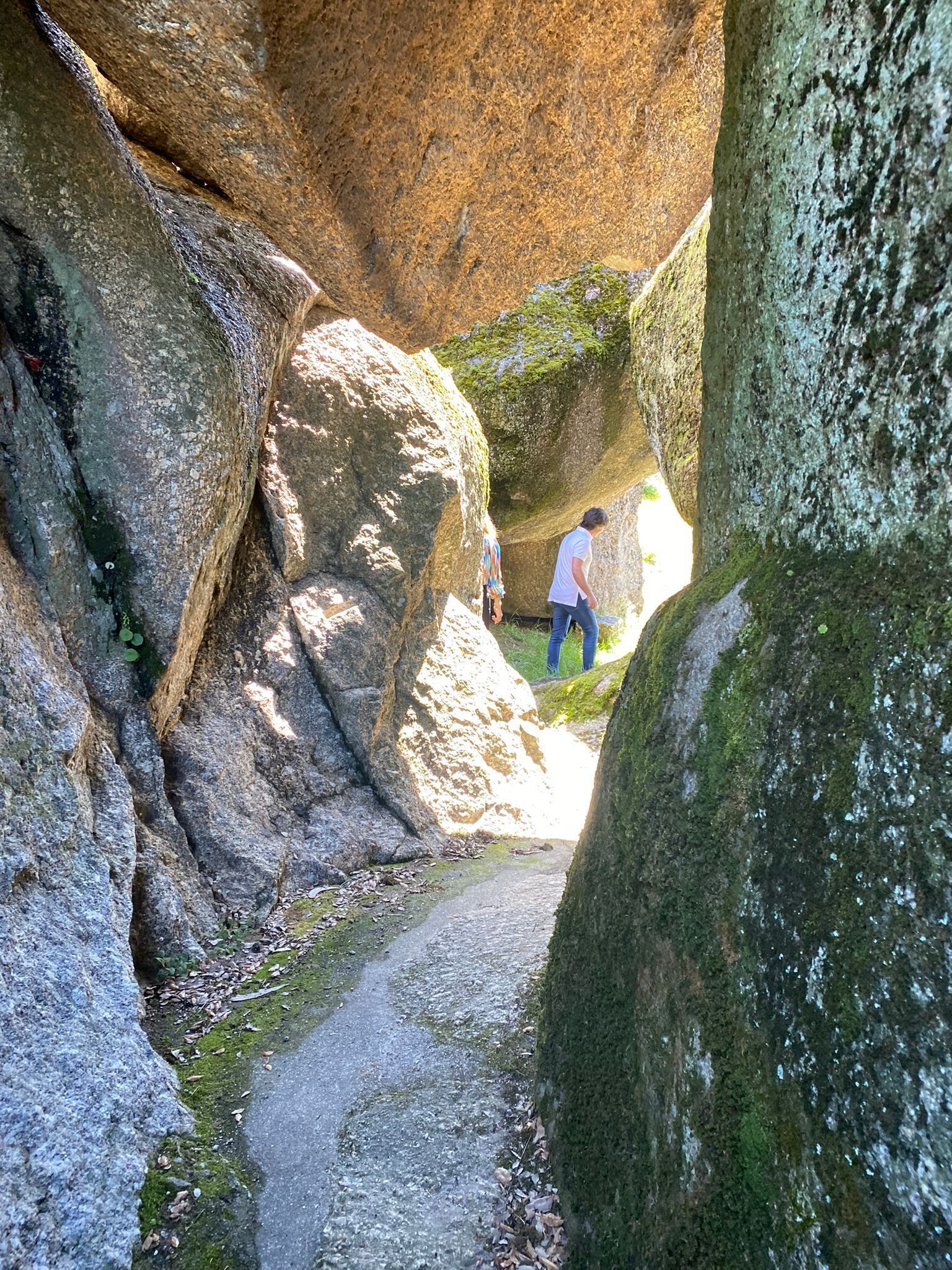 Un sentier étroit entre de gros rochers, sur lequel une personne s’éloigne de la caméra.